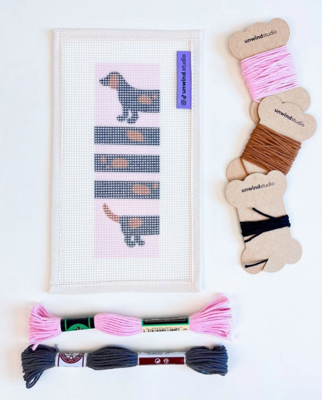 "WI(E)NNER BOOKMARK NEEDLE STICH KIT " UNWIND STUDIO Kit ponto cruz com desenho de cão em tela branca e novelos de linhas coloridas