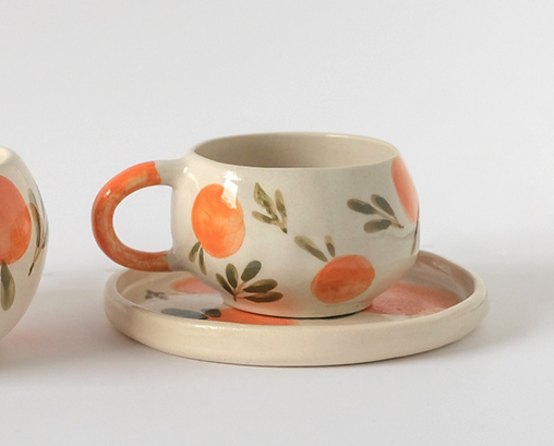 CHÁVENA CITRUS MANU SOUZA chávena de cerâmica com padrão de laranjas e folhas verdes sobre prato