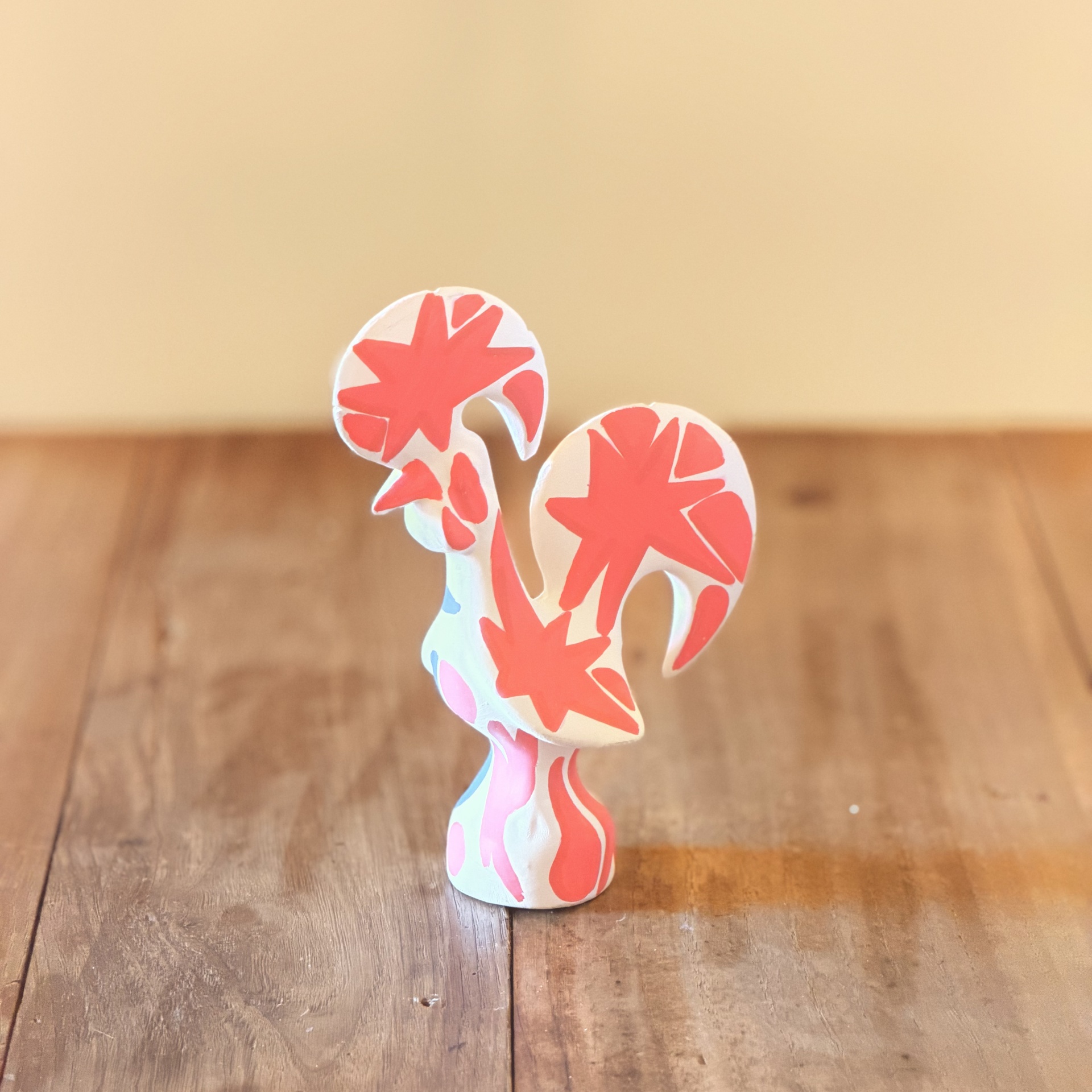 GALO DE BARCELOS 15 CM ZEROS TATTOO Escultura de cerâmica branca com padrões vermelhos e rosas colocada numa superfície de madeira.