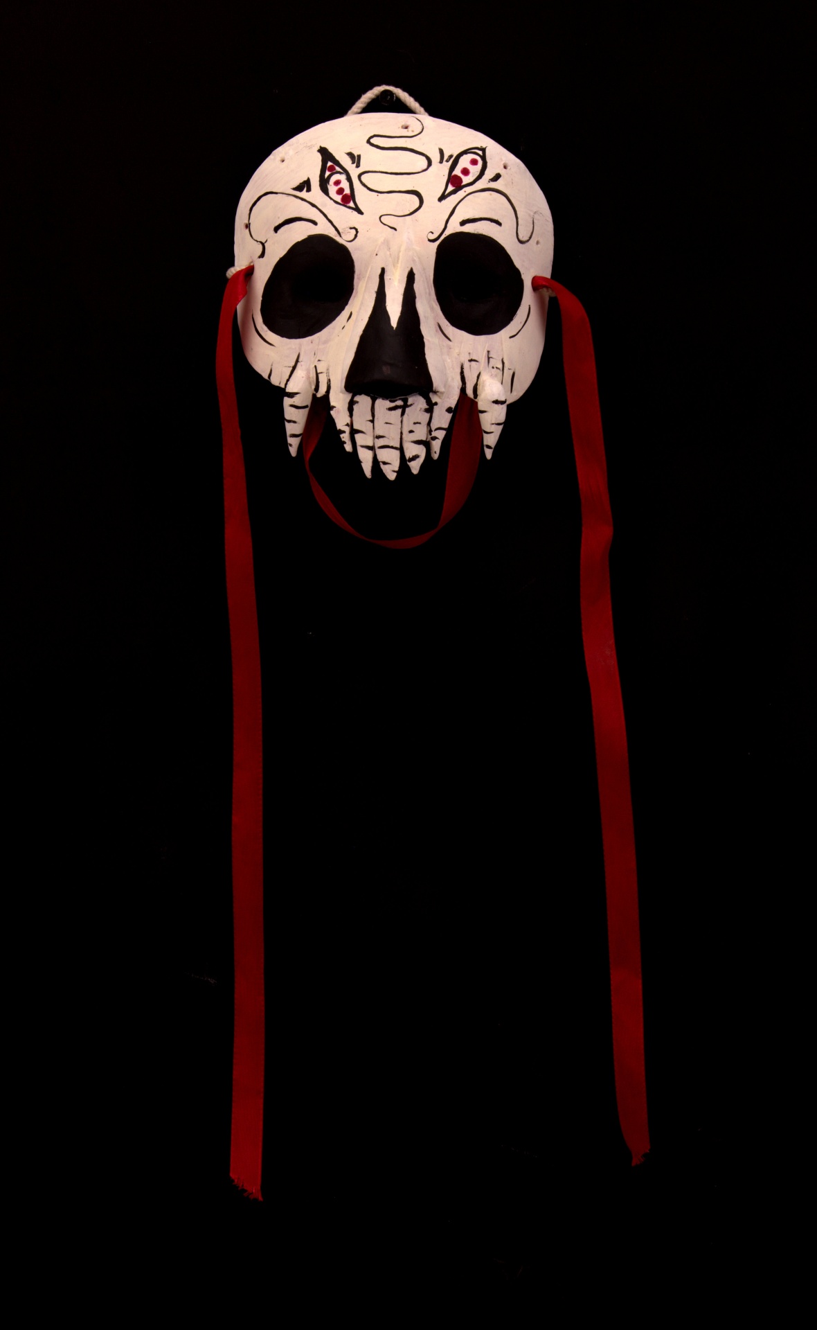 MÁSCARA "MORTE" ANDREIA PINHO Máscara branca de caveira com detalhes pretos e vermelhos e fitas vermelhas longas.