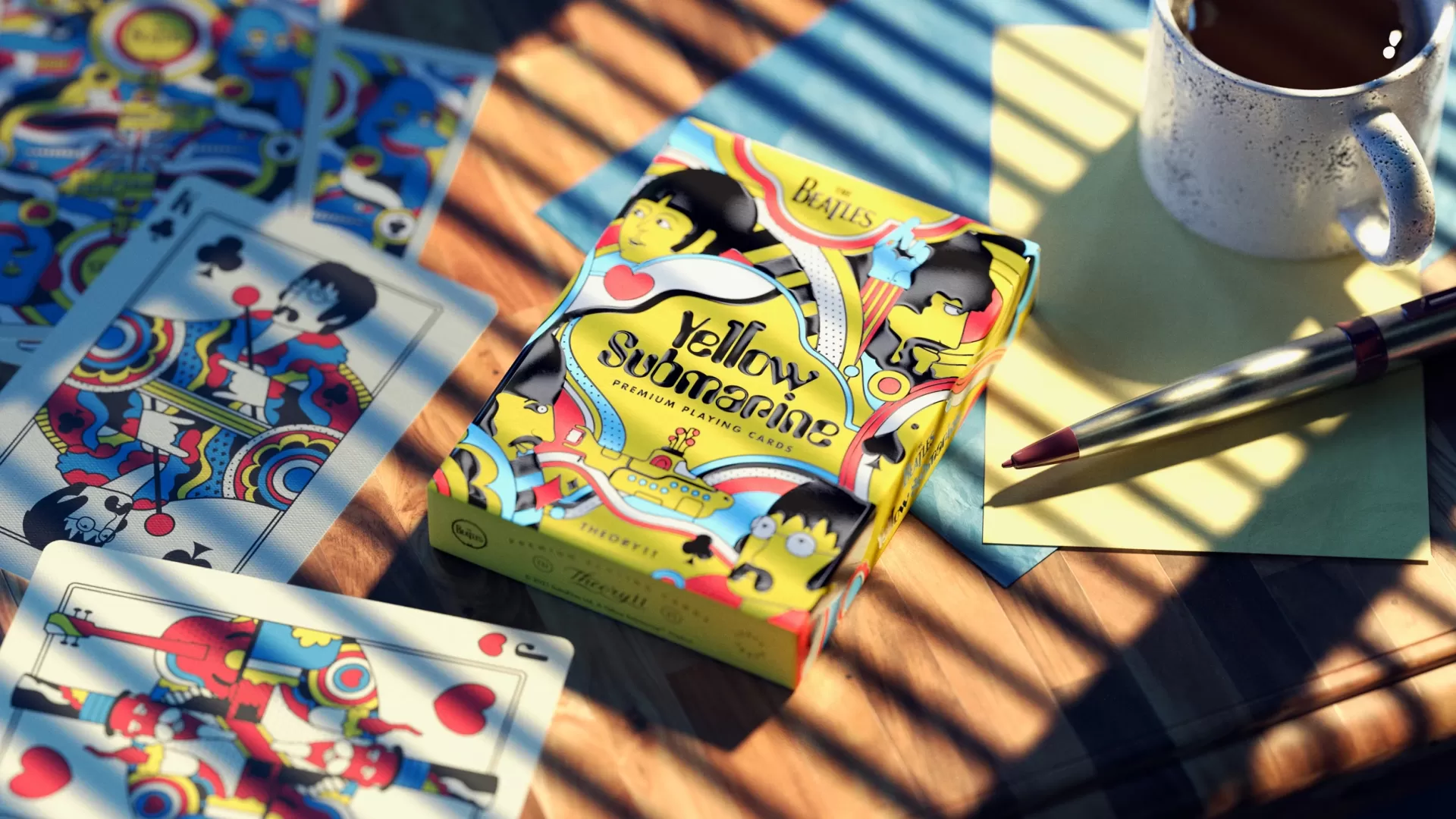 BARALHO DE CARTAS "YELLOW SUBMARINE, THE BEATLES " THEORY11 CARDSHOUSE Baralho de cartas colorido Yellow Submarine dos Beatles com caneca e caneta ao lado.