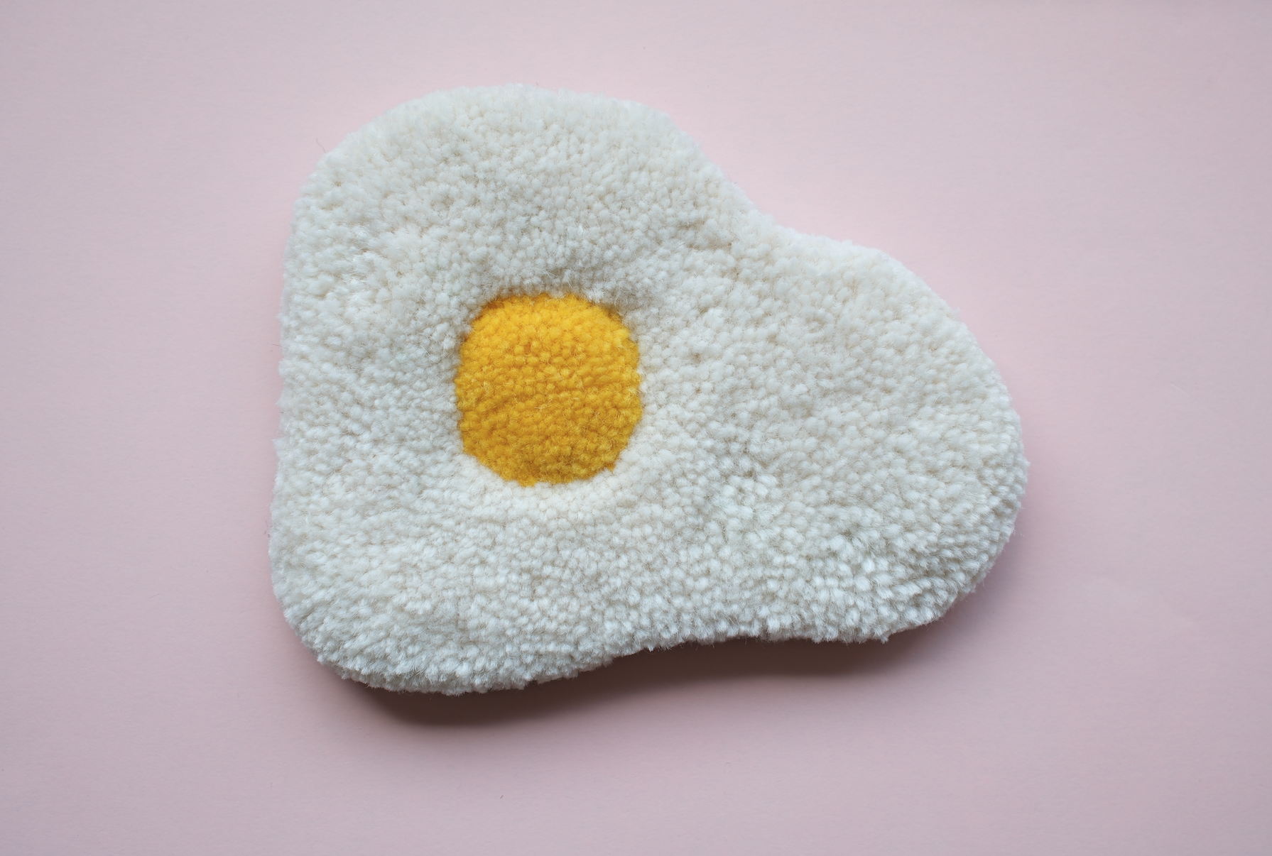 PEÇA TUFTING "OVO" KIKA tapete ou almofada felpuda branca com centro amarelo sobre fundo rosa