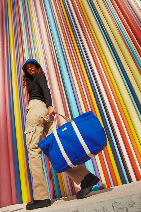 MALA JEAN HINDBAG Mulher com mala azul e parede colorida às riscas verticais