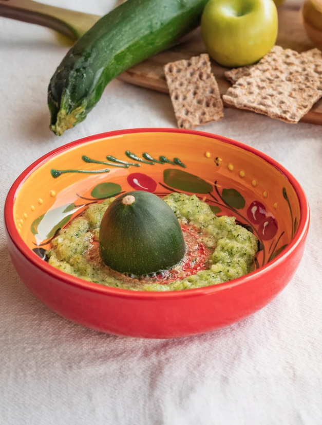 TAÇA RALADOR GRANDE "PROVENÇAL" ALFAR TIERRA COCIDA Tigela de cerâmica vermelha e amarela com curgete e puré verde, maçã, bolachas e tábua de madeira ao fundo