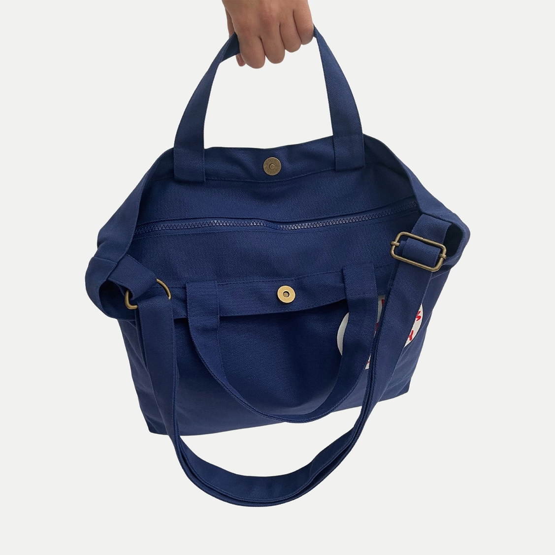 BOLSA "THE MOON MAKES US CRAZY" - DAVID SHRIGLEY Mala azul escura em tecido com fecho de correr e botão de pressão, com duas pegas e uma alça ajustável.