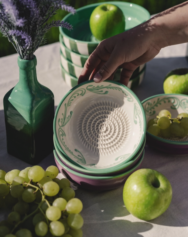 TAÇA RALADOR MÉDIA "VINTAGE ESMERALDA ALFAR TIERRA COCIDA Tigelas de cerâmica decoradas, maçãs verdes, uvas e um vaso verde com flores lilases sobre mesa ao ar livre
