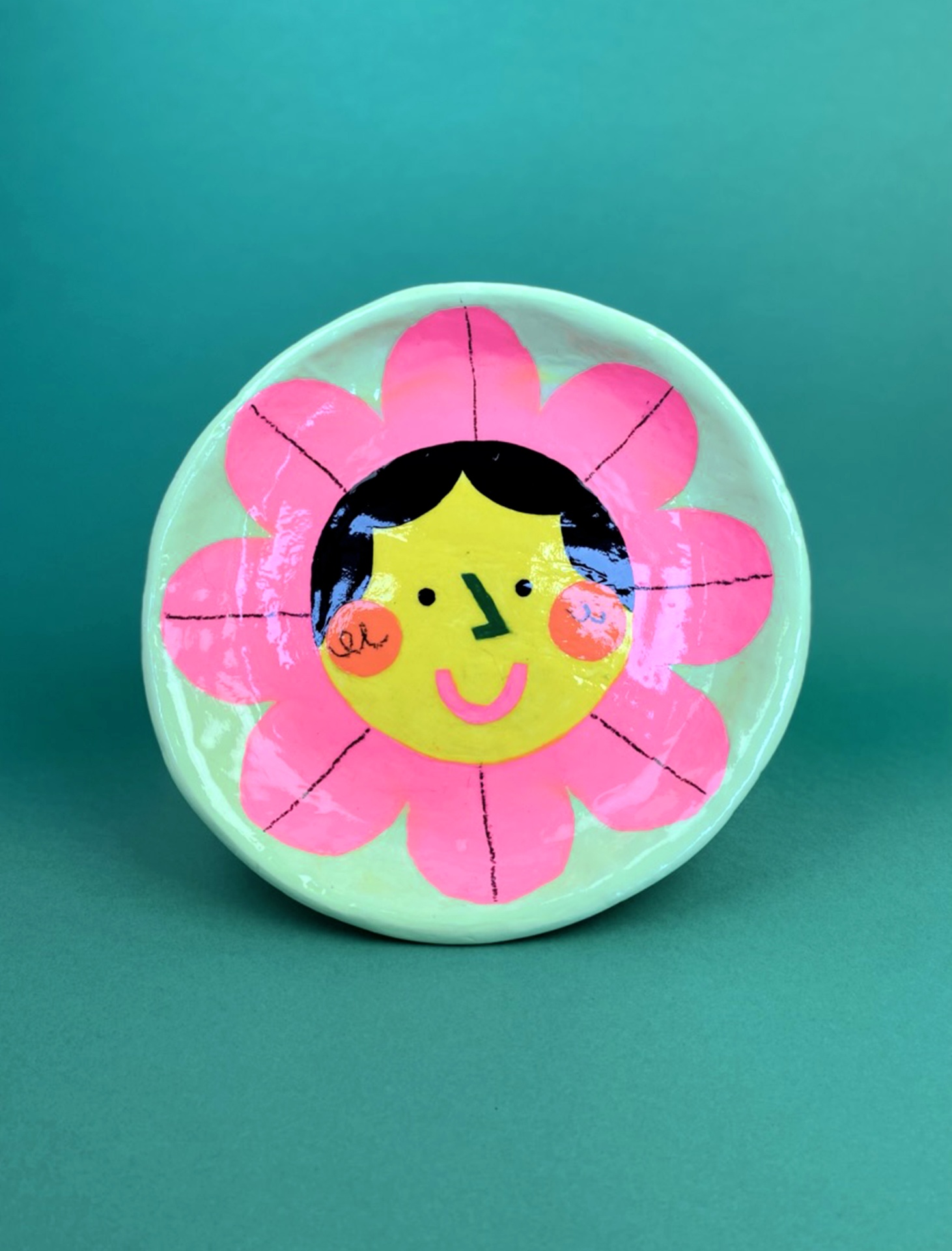 PRATO EM ARGILA "PALMIRA" CATPIVARA Prato de cerâmica redondo com desenho de flor sorridente em rosa e amarelo