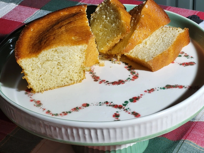 SUPORTE PARA BOLO XMAS TÁLIA PÓ DE BARRO Bolo cortado em fatias num prato branco com padrões florais sobre uma mesa com toalha vermelha e verde
