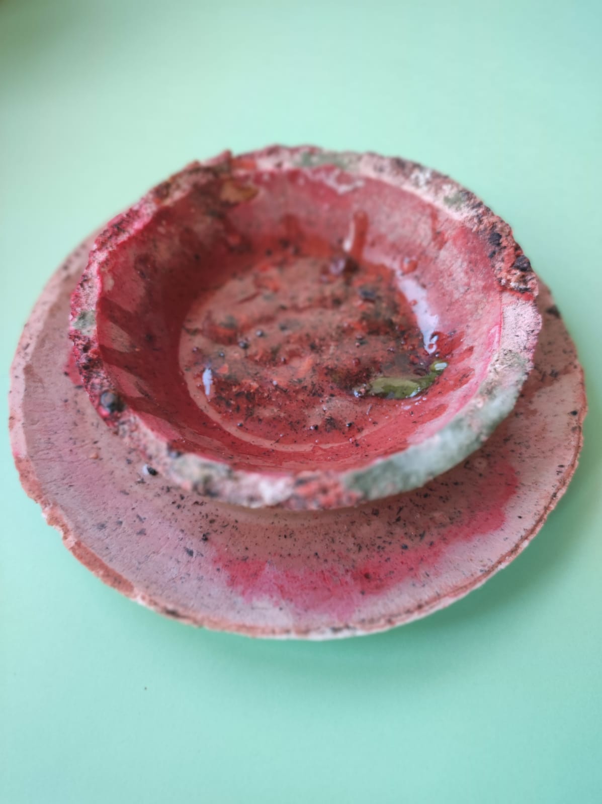 CONJUNTO ROSA DE CHÁ INGLÊS "TABLEWARE FOR ISOLATION" MARQUES MARQUES Conjunto de prato e taça de cerâmica vermelhos desgastados sobre superfície verde