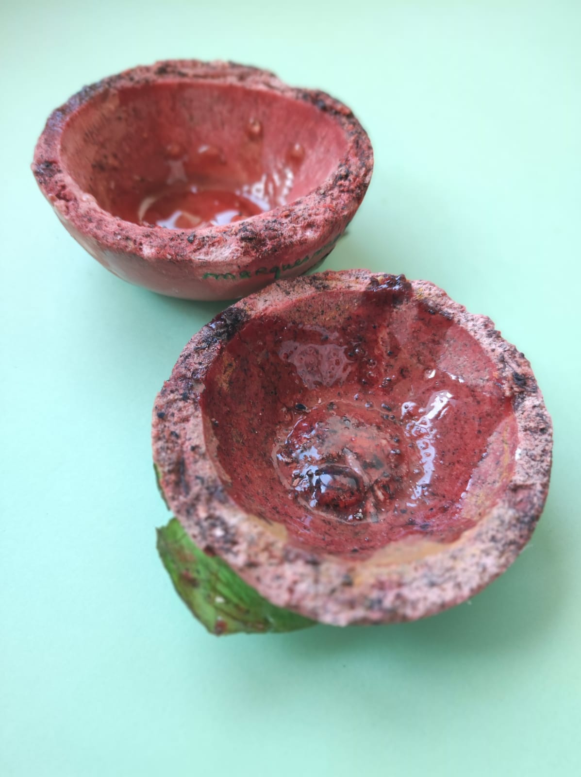 CONJUNTO DE 2 XÍCARAS DE CAFÉ "TABLEWARE FOR ISOLATION" MARQUES MARQUES Dois frutos castanha avermelhada abertos com interior vermelho brilhante sobre fundo verde claro
