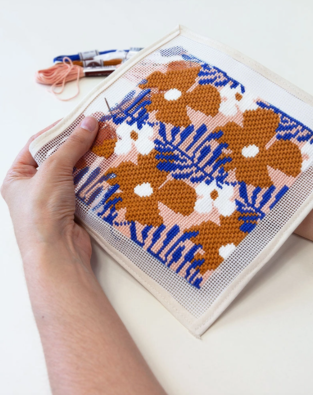 "KIT ESTOJO PARA ÓCULOS DE SOL" ROYAN UNWIND STUDIO Bordado em tela aida com flores castanhas e folhas azuis nas mãos