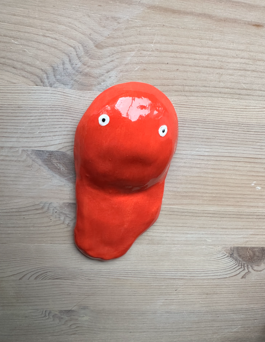 PAINT BLOB RED CERAMICA KIKA Objeto decorativo vermelho com olhos pintados sobre madeira clara