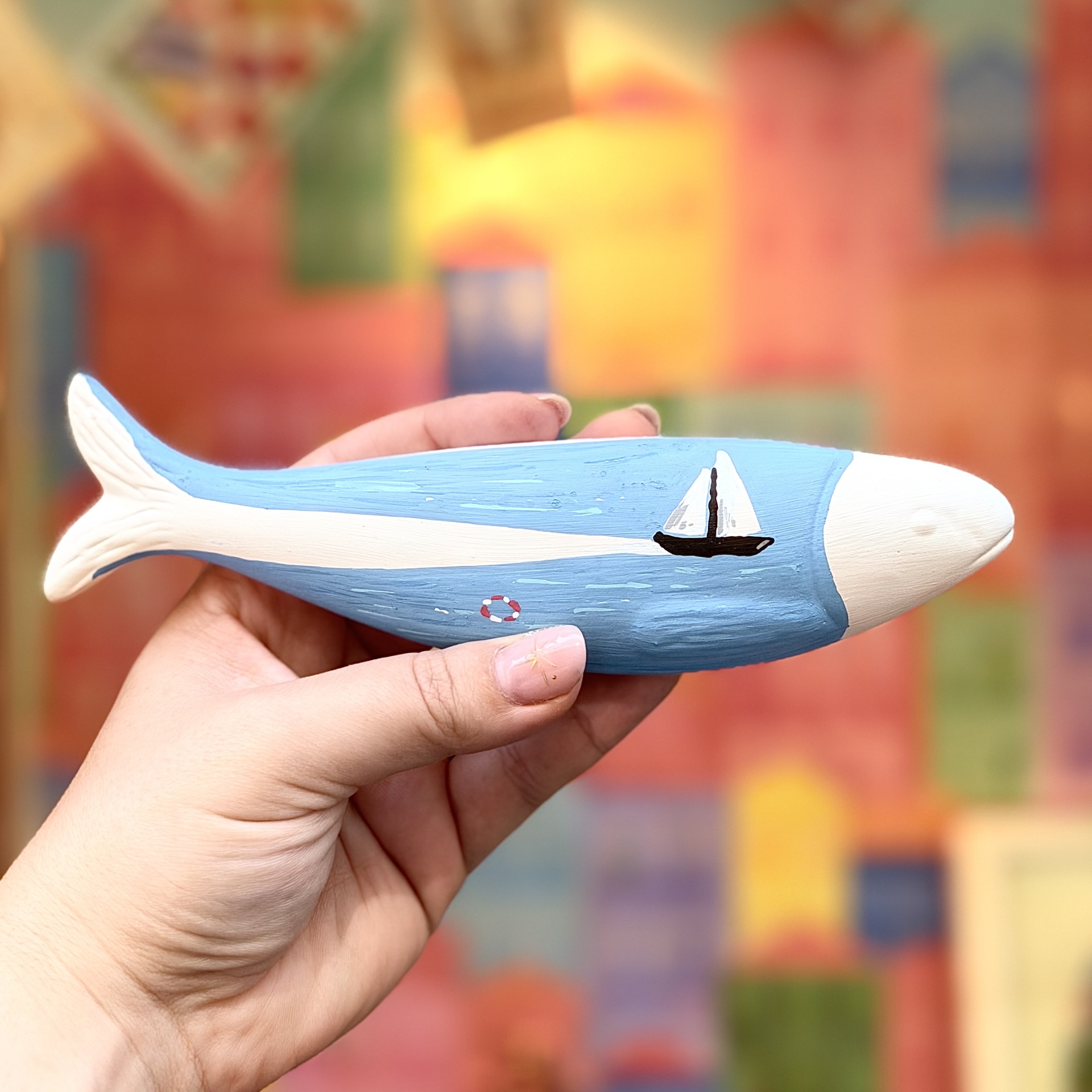 SARDINHA GRANDE ZEROS TATTOO Figura de peixe decorativo azul e branco com barco pintado na lateral, segurado por uma mão