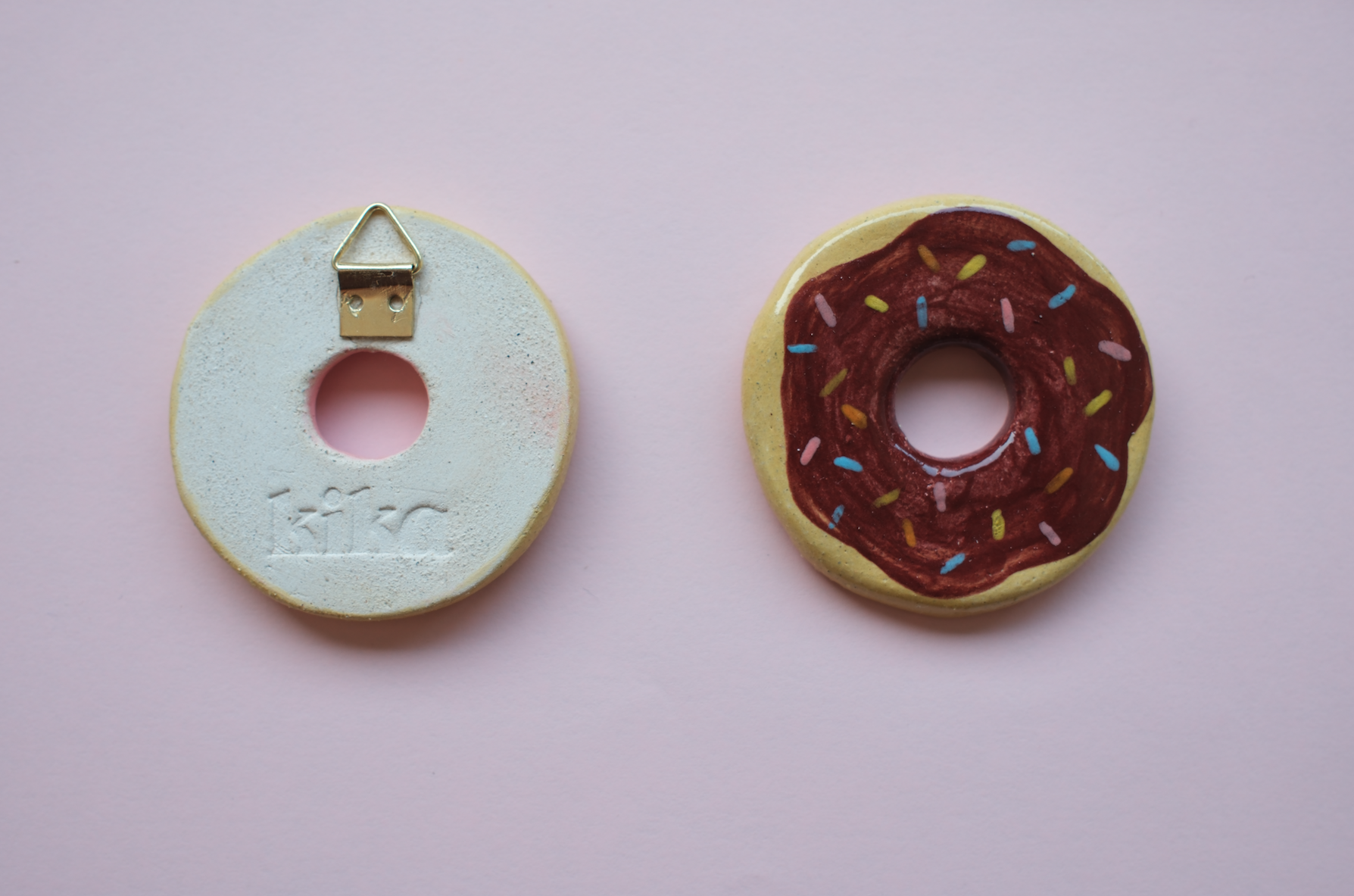 PEÇAS DE CERÂMICA "BREAKFAST FOR DINNER" KIKA Objetos redondos em cerâmica, um com design de donut e outro com suporte metálico e inscrição