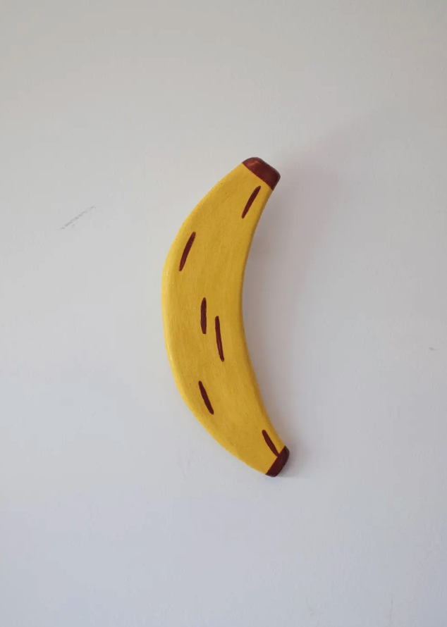 PEÇAS DE CERÂMICA "BREAKFAST FOR DINNER" KIKA Banana decorativa amarela de madeira numa parede branca