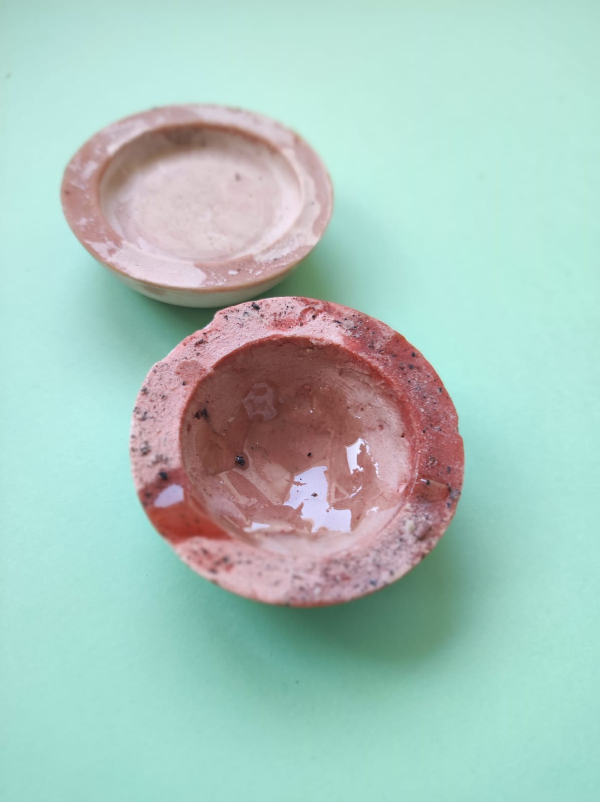 CONJUNTO DE 2 MALGAS PARA GINJINHA "TABLEWARE FOR ISOLATION" MARQUES MARQUES Dois cinzeiros redondos em cerâmica, um bege e outro vermelho, sobre superfície verde clara