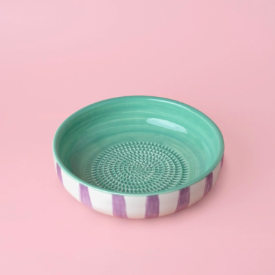 Prato cerâmico verde turquesa com riscas lilás sobre fundo rosa