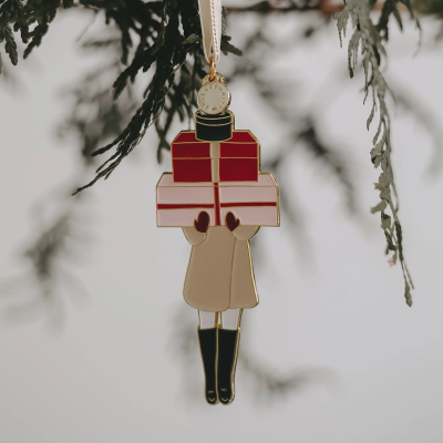 Enfeite de figura humana segurando presentes pendurado em ramo verde.