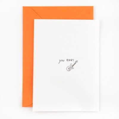 Cartão branco com guitarra desenhada e texto 'you ROCK!' com envelope laranja atrás