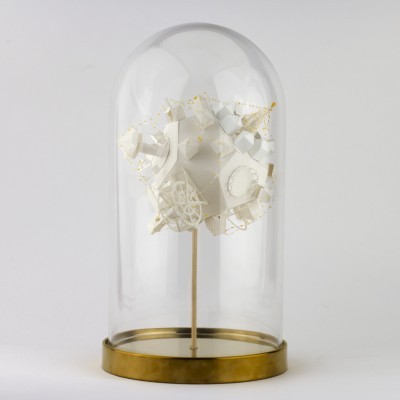 Objeto decorativo branco e dourado numa campânula de vidro com base metálica dourada