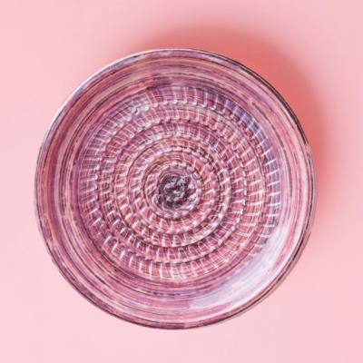 Prato cerâmico púrpura com padrão circular texturizado sobre fundo rosa