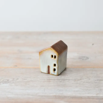 Escultura pequena de casa em cerâmica castanha e creme sobre mesa de madeira clara