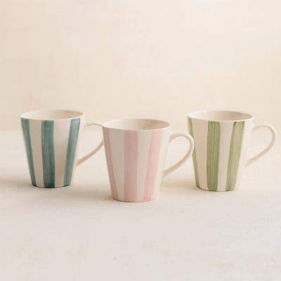 Três canecas cerâmicas listradas azul, rosa e verde sobre fundo branco