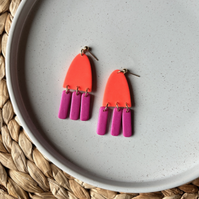 Brincos geométricos laranja e roxo em prato branco