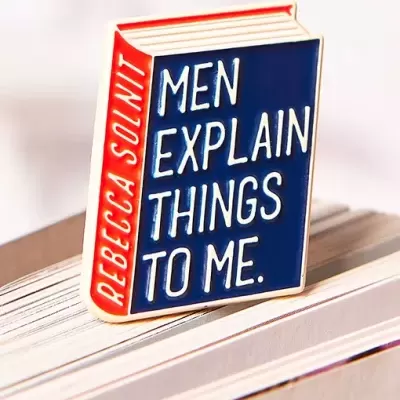 Pin de esmalte em forma de livro com texto branco em fundo azul e lateral vermelha