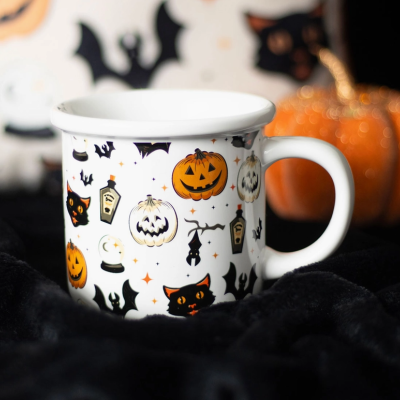 Caneca branca de Halloween com desenhos coloridos e abóbora decorativa ao fundo