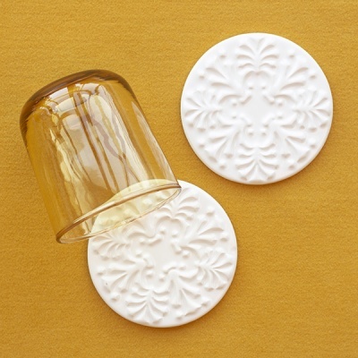 Descanso para copo branco com padrão floral em relevo e copo de vidro âmbar