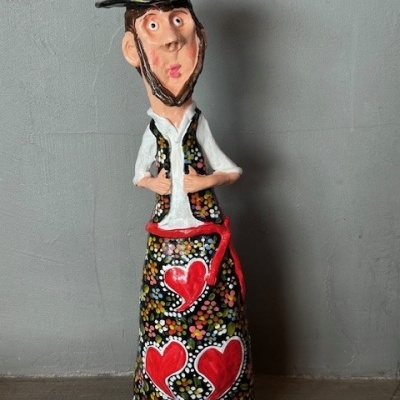 Estátua de cerâmica de homem com chapéu e saia decorados com padrões florais e corações vermelhos