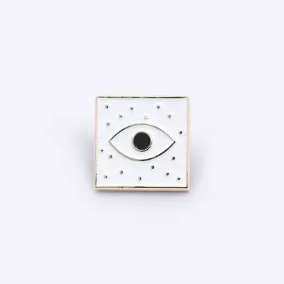 Pino quadrado branco com desenho de olho e bolinhas douradas.