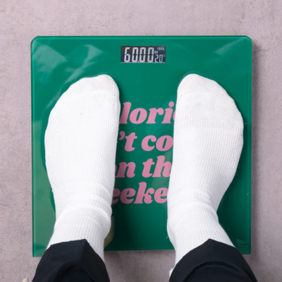 Balança digital verde com pés de meias brancas e ecrã mostrando peso e temperatura