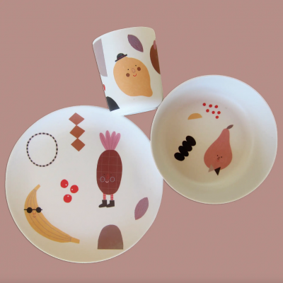 Conjunto infantil de cerâmica com desenhos de frutas sorridentes em fundo rosa.