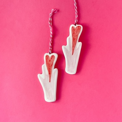 Dois ornamentos em forma de mão branca com desenhos vermelhos e cordões cor-de-rosa e branco