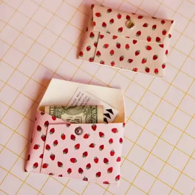 Carteiras pequenas brancas com padrão de morangos vermelhos e botão de coração sobre superfície branca com linhas amarelas