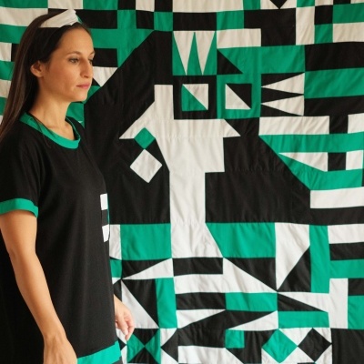 Mulher com t-shirt preta com detalhes verdes e padrão geométrico ao fundo