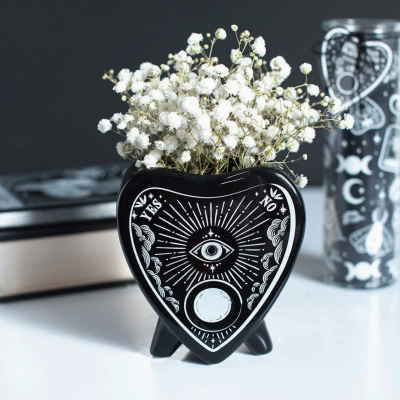 Vaso de cerâmica preto em forma de coração com desenho branco e flores brancas.