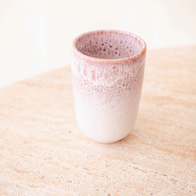 Copo cerâmico branco com detalhes rosa avermelhado sobre mesa de madeira clara