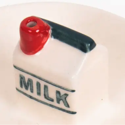 Objeto cerâmico decorativo com texto MILK, bico vermelho e tampa preta