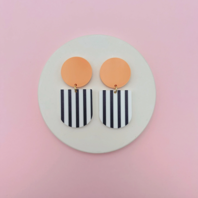 Brincos laranja e listrados apresentados em fundo rosa.