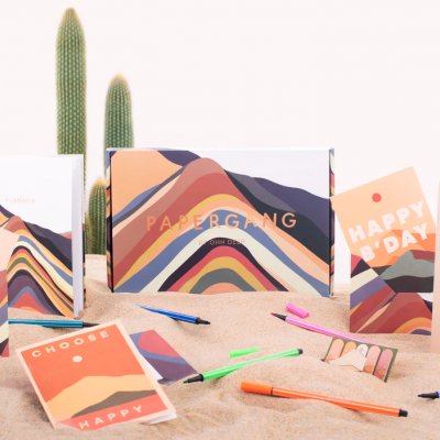 Conjunto de papelaria com motivos de montanhas coloridas, canetas e cactos ao fundo