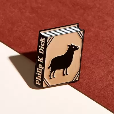 Pin metálico em forma de livro com uma ovelha na capa e o nome Philip K Dick na lombada