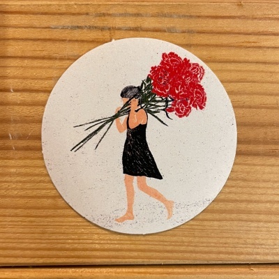 Adesivo redondo com mulher de vestido preto e flores vermelhas sobre madeira clara