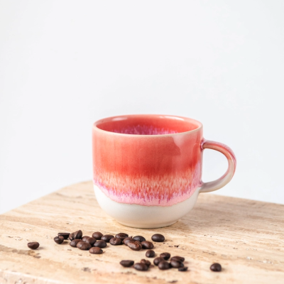 Caneca vermelha e branca em cerâmica com grãos de café sobre madeira clara