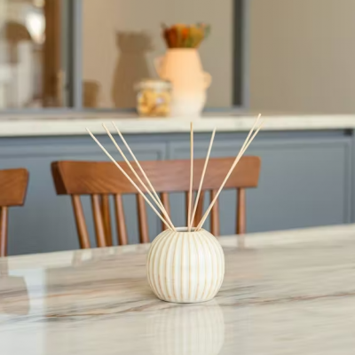 Difusor de aroma cerâmico branco riscado dourado com varetas de madeira numa mesa de mármore