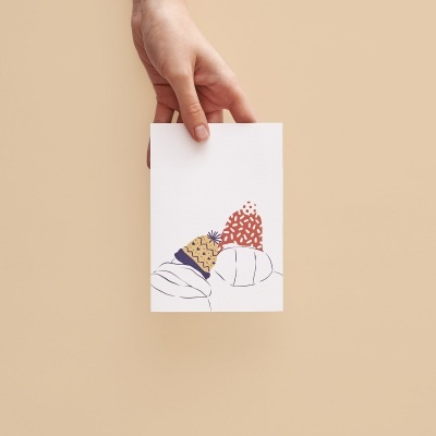 Cartão branco com ilustração colorida abstrata segurado por uma mão sobre fundo bege