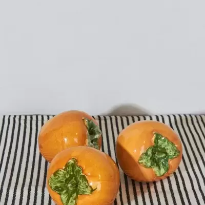 Três caquis laranja com folhas verdes sobre tecido riscado preto e branco