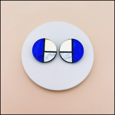 Brincos redondos azul, branco e prateado sobre prato branco